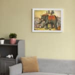 Vintage wall art of a grand elephant parade with red and gold decorations, surrounded by people in a festive village scene. displayed on the wall in a white frame