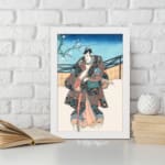 Vintage wall art of a Japanese samurai in a floral kimono standing in a peaceful winter scene with a snowy backdrop and a tree branch. displayed on the wall in a white frame