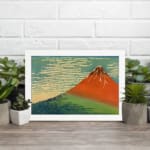 Infidu vintage wall art featuring an iconic view of Mount Fuji with a red-orange peak, a blue sky, and lush green surroundings in a traditional Japanese style. displayed on the wall art in a white frame