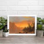 Vintage wall art of a tranquil sunset lake with warm tones, towering cliffs, and lush trees, creating a serene and timeless landscape. displayed on the wall in a white frame