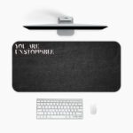 Infidu black desk pad with bold white "YOU ARE UNSTOPPABLE" text on a textured black background.