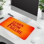 Infidu desk pad with bold red "Learn From Failure" quote on an orange to red gradient background.